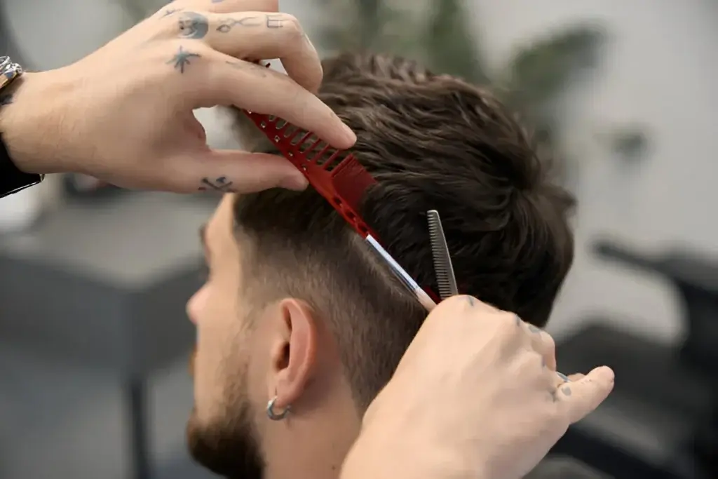 Barber styling a man's hair with scissors and comb, demonstrating modern men's hairstyles.