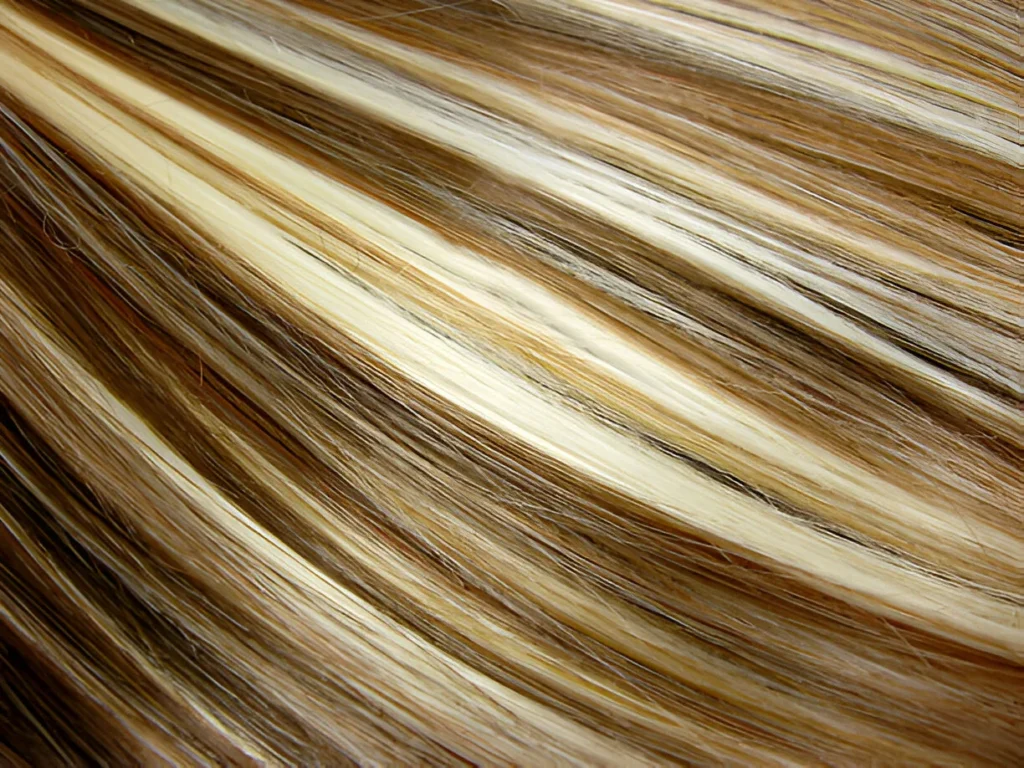 A close-up of dark brown hair with highlights, featuring blonde streaks that create a flowing, multi-tonal effect with a glossy finish.