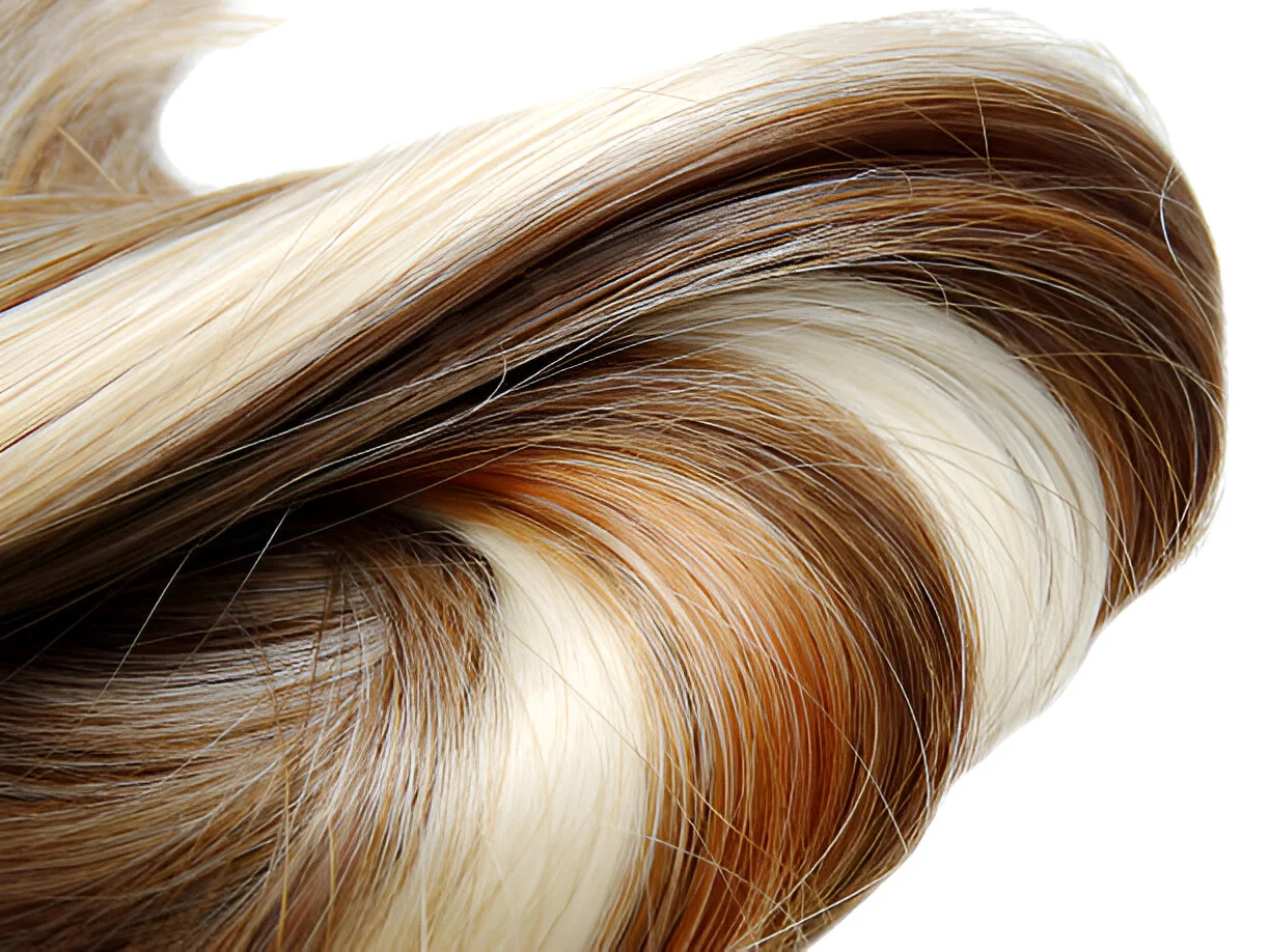 A close-up of dark brown hair with highlights, featuring a mix of blonde and light brown streaks, creating a wavy, multi-tonal effect against a white background.