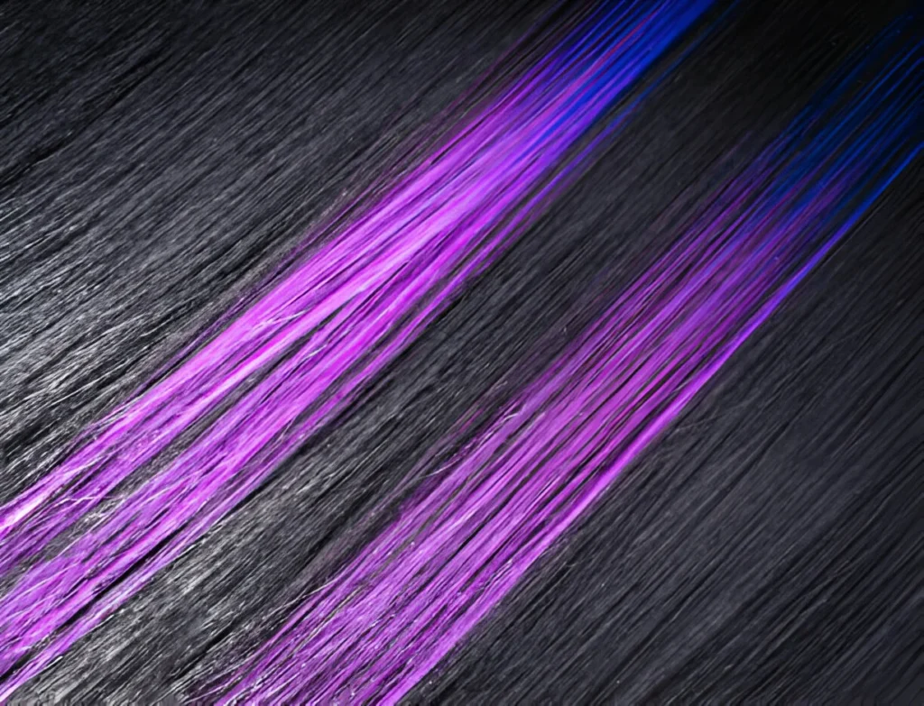 A close-up of black hair with highlights, featuring vibrant purple streaks that contrast sharply against the dark base, creating a bold, dynamic look.