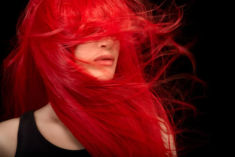 A woman with vibrant red hair dye flowing freely against a black background, wearing a black sleeveless top.