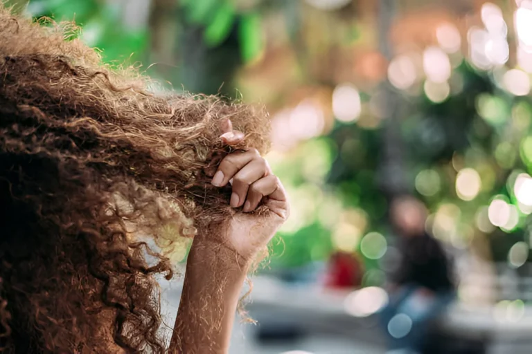 Close-up of hand holding tangled, dry high porosity curly hair in natural sunlight.